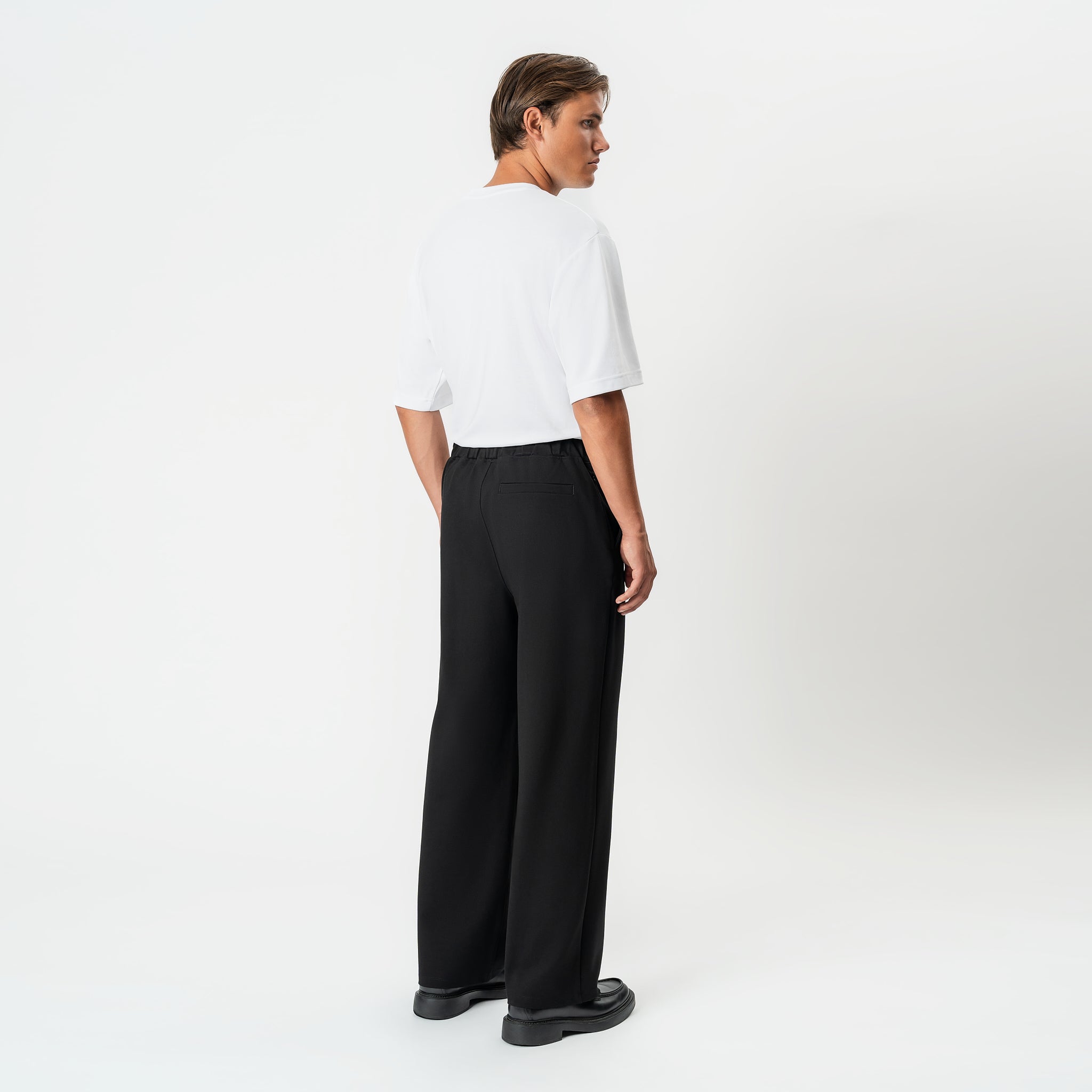 Angled back view of the black Socrates wide-leg pleated pant